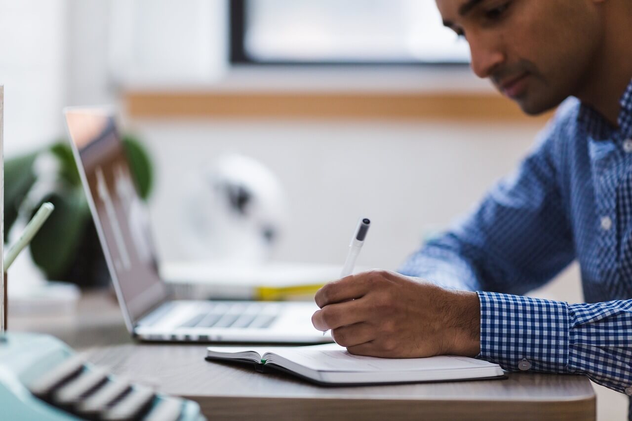 man writing next to a laptop