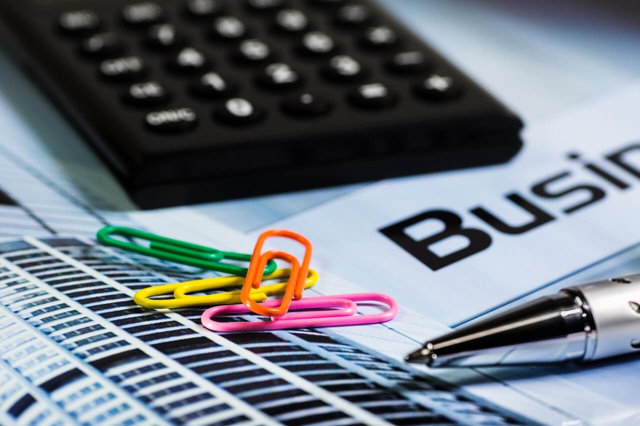 Une calculatrice, un stylo et des trombones posés sur un bulletin de salaire